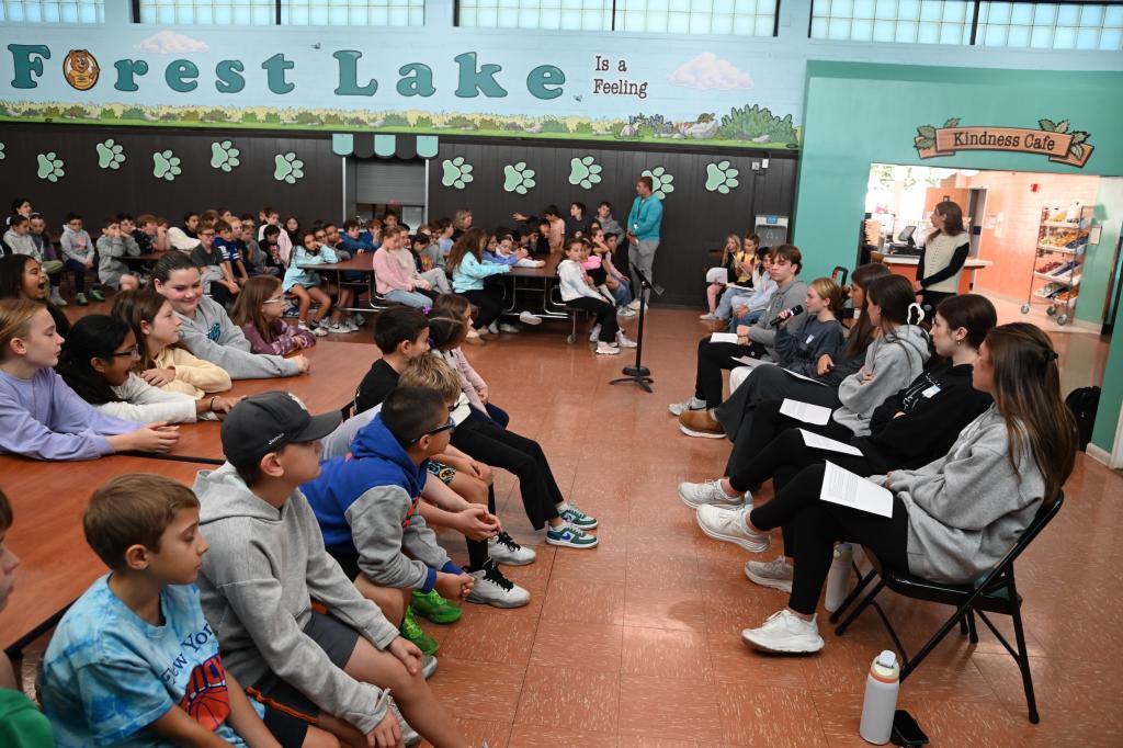 A group of students sits facing a panel of speakers in a school cafeteria.